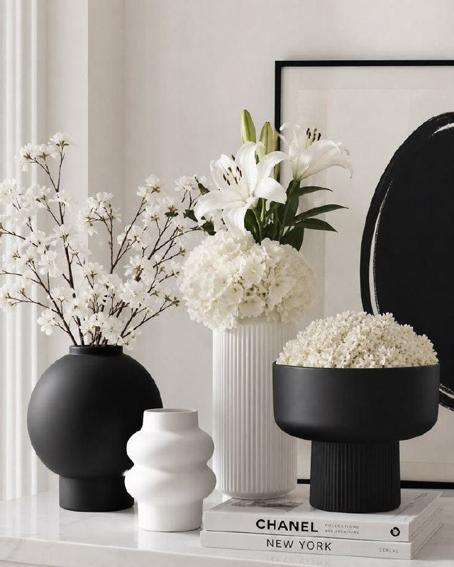 faux hanging plant in black pot among decorative vases and white flowers on a stylish table.